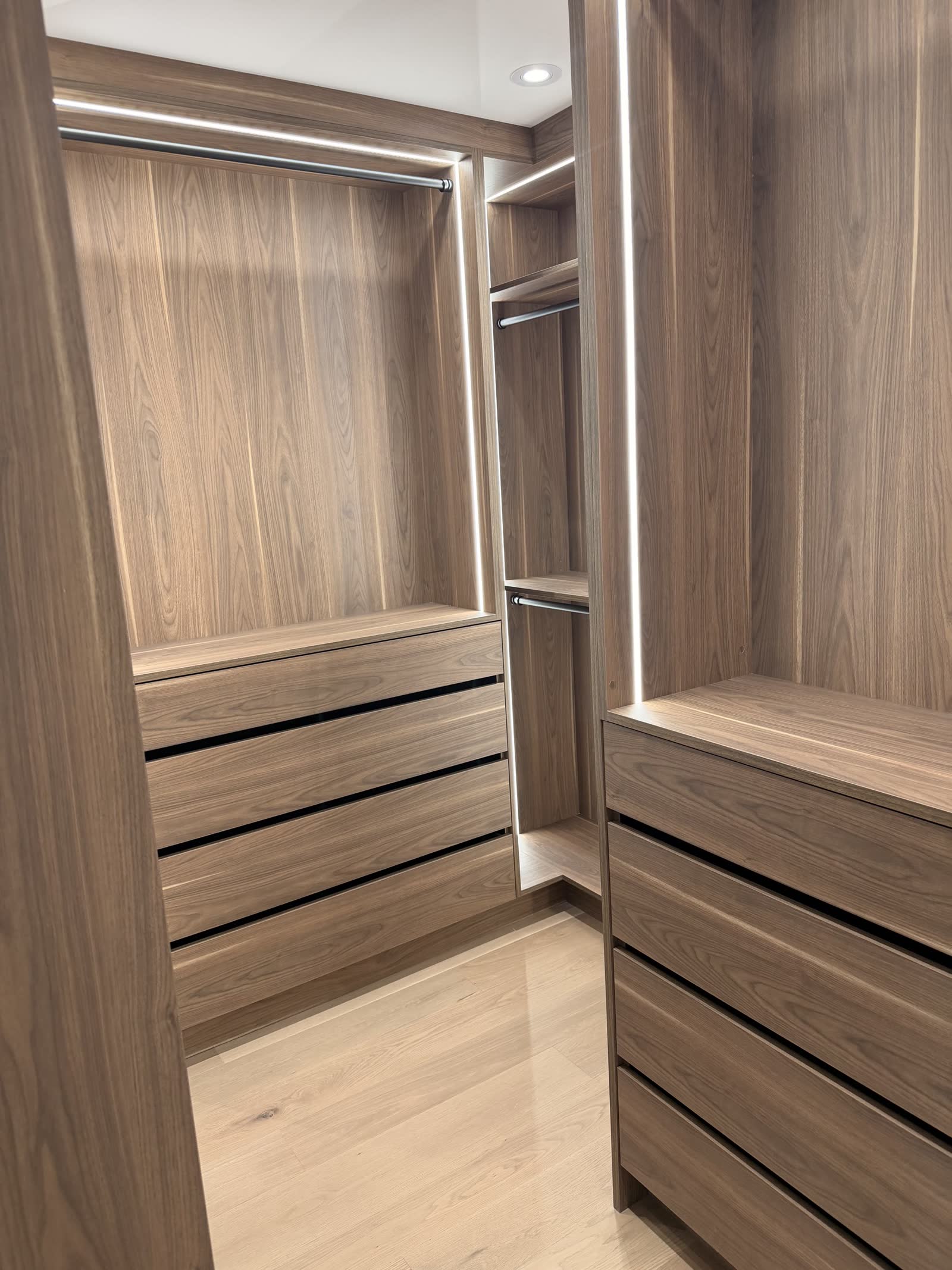Walnut walk-in closet with lit hanging rails and dovetailed drawer banks