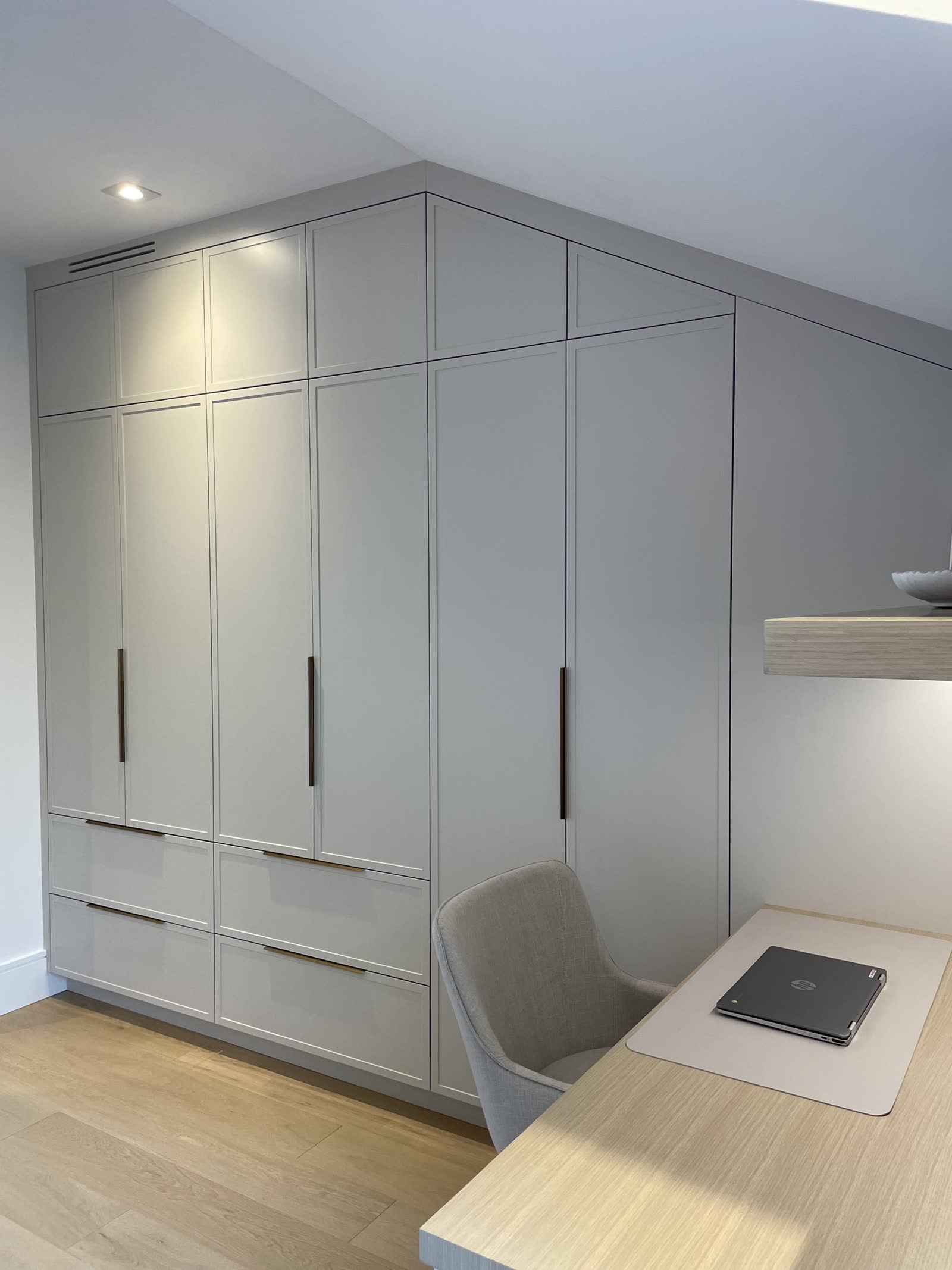 Fitted wardrobes following a sloped ceiling beside a built-in desk