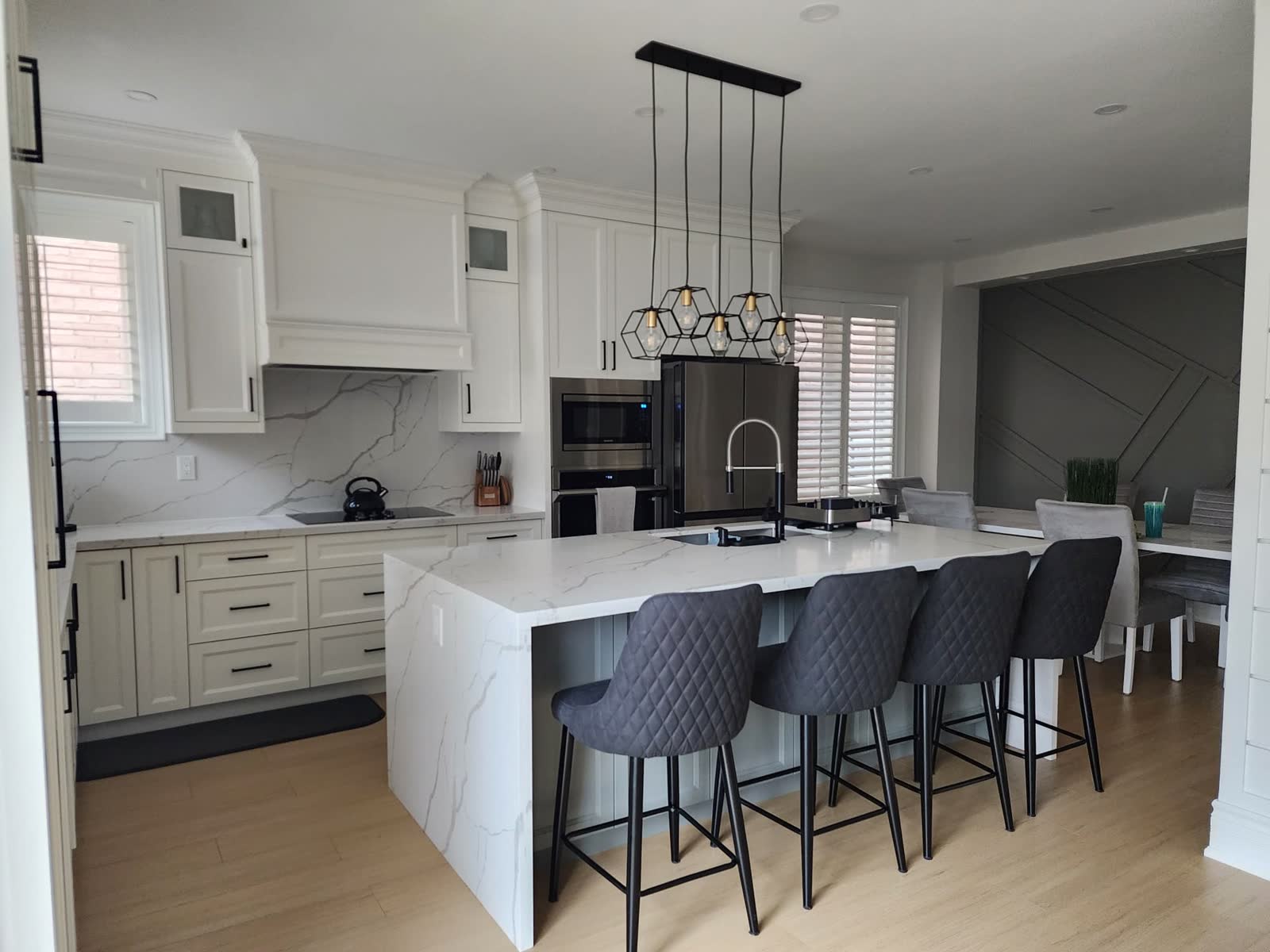 White kitchen with a marble island, pendant lighting and a panelled hood surround