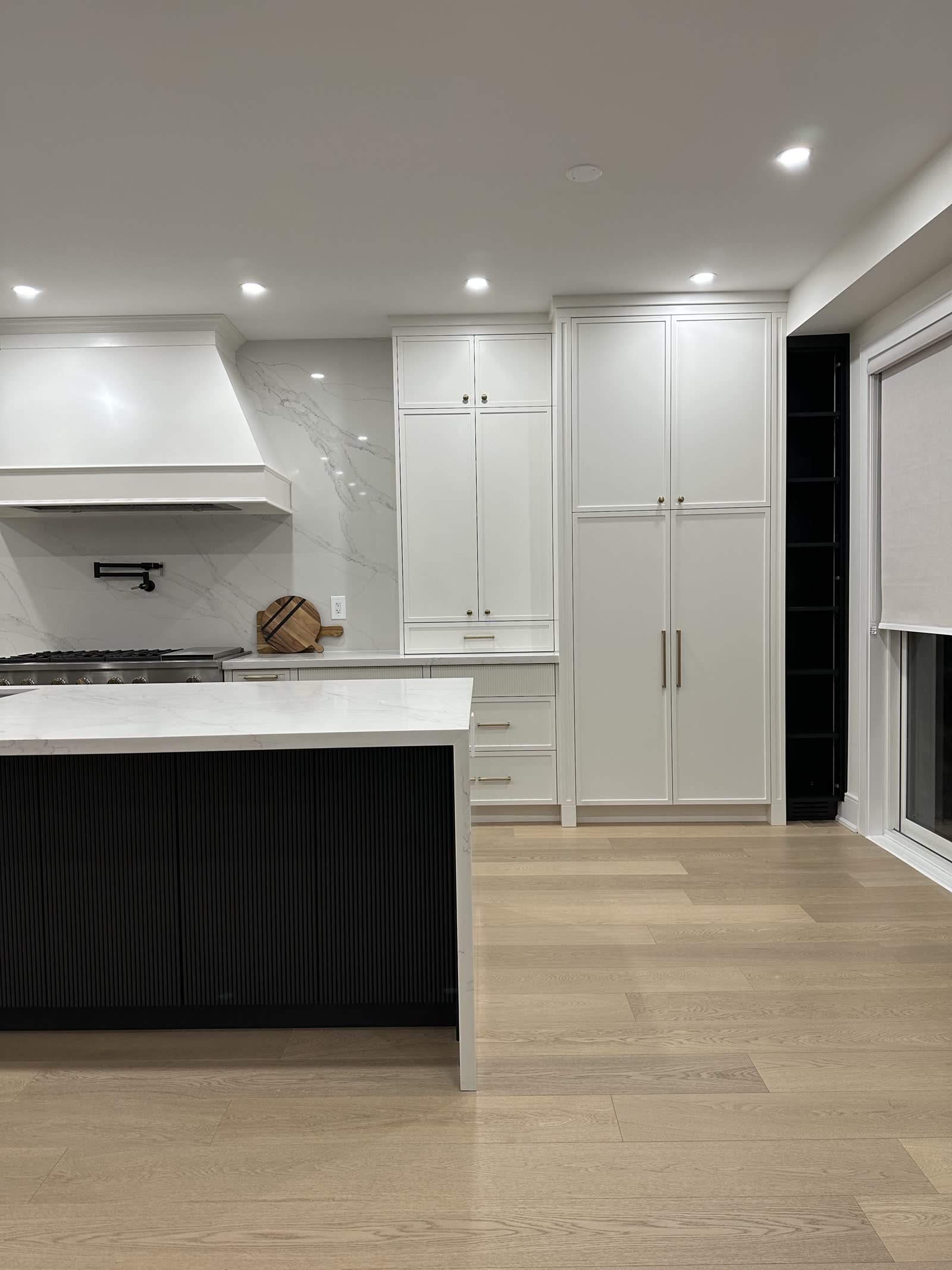 White inset kitchen with a black fluted island, marble counters and a panelled hood surround